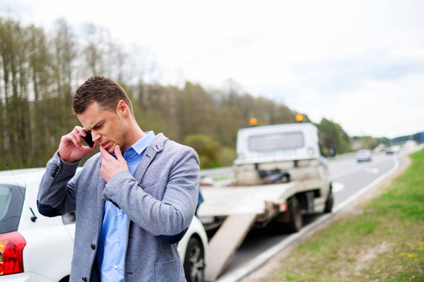 Hombre llamando mientras la grúa recoge su coche roto
 - Foto, imagen