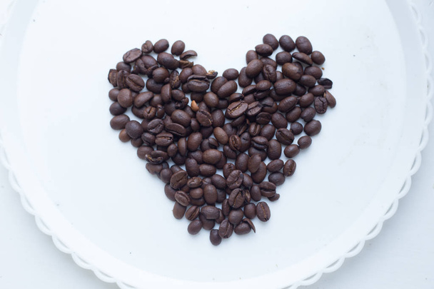 Κόκκους καφέ σε μορφή της καρδιάς σε όμορφο φόντο. Αγάπη. Insparation. Στο άσπρο πιάτο. - Φωτογραφία, εικόνα