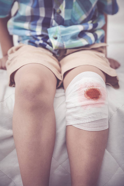 Παιδί τραυματίστηκε. Τραύμα στο γόνατο του παιδιού με επίδεσμο. Εφέ Βίντατζ τόνος. - Φωτογραφία, εικόνα