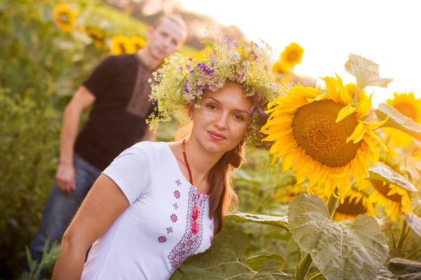 Jonge mooie verliefde paar in de nationale Oekraïense shirts bij zonsondergang te wandelen in een gebied van bloeiende zonnebloemen - Foto, afbeelding