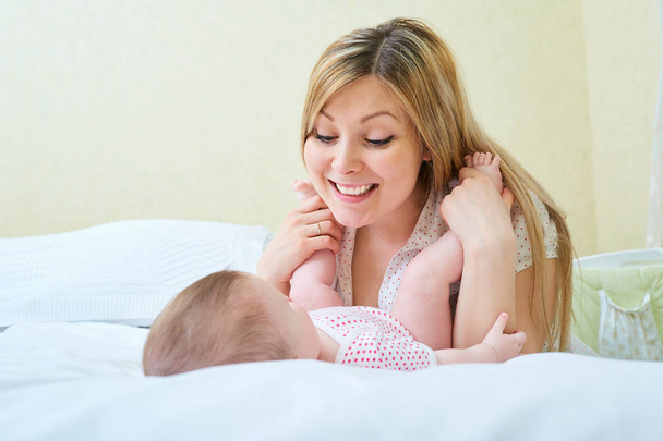 Mother playing with her baby on the bed. Mom smiles to her child - Foto, Bild