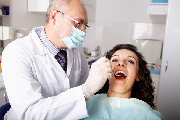 Dentist with mirror checking patient's teeth - Fotoğraf, Görsel