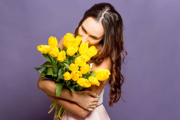 Młoda piękna kobieta trzyma Bukiet żółtych tulipanów. Wiosna. - Zdjęcie, obraz