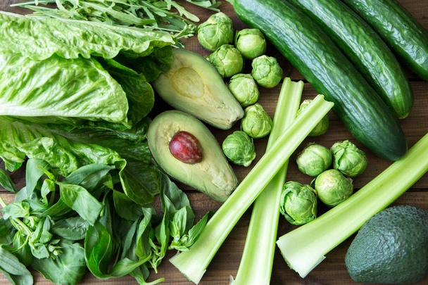 Products containing folic acid - B9 vitamin . Green vegetables on wooden background. Celery, arugula, avocado, Brussels sprouts, basil, cucumber, romaine salad - 写真・画像