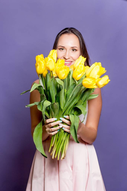 Young beautiful woman holding a bouquet of yellow tulips. Spring. - Photo, image