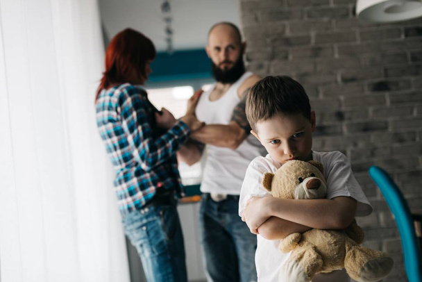 Üzgün çocuk oyuncak ayısını ebeveynler kavga sırasında sarılma. - Fotoğraf, Görsel