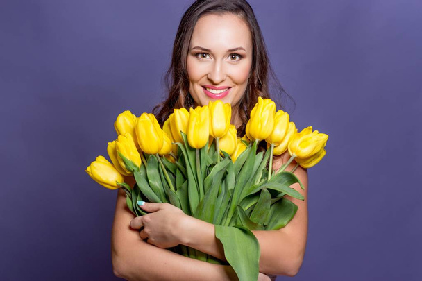 Young beautiful woman holding a bouquet of yellow tulips. Spring. - 写真・画像