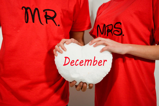 young couple in red shirts holding white fabric heart with text - Photo, Image