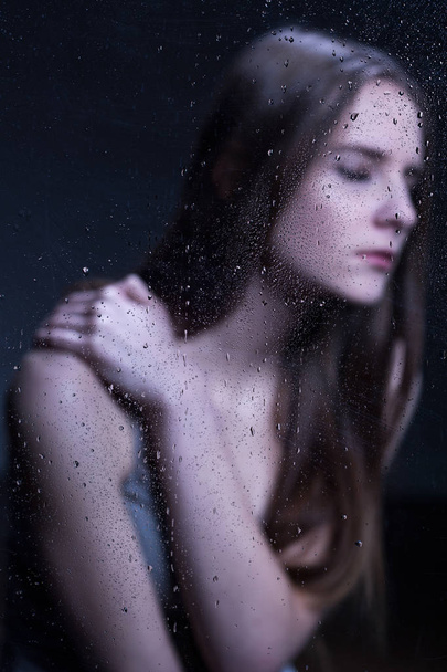 Young, sad woman behind glass - 写真・画像