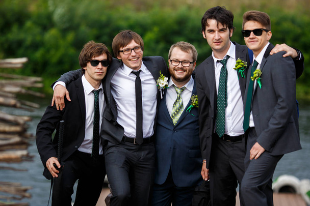 Stylish dressed groom and groomsmen pose together by the river  - Foto, imagen