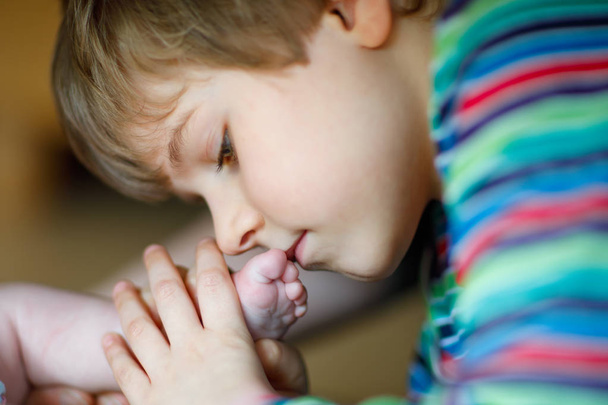 Маленький хлопчик цілується і грає з ногами новонародженої дитини
. - Фото, зображення