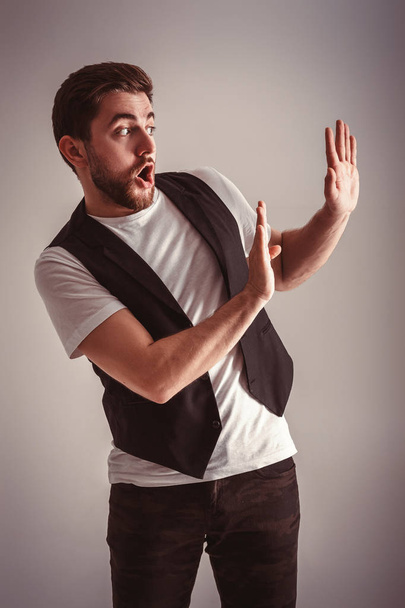 cute young frightened man with beard in shirt and waistcoat over gray background - Photo, image