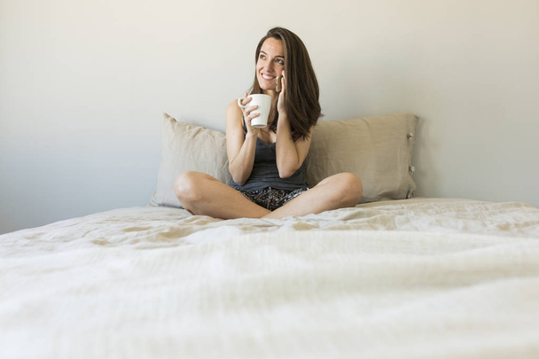 beautiful young woman enjoying coffee on bed - Foto, Imagen