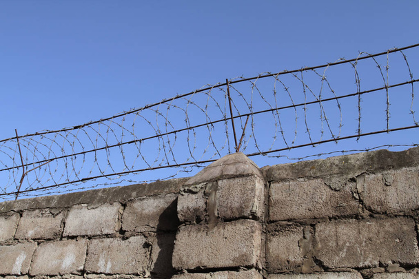 Drut kolczasty na szczycie ceglanego muru ogranicza swobodny przepływ ludzi i chroni nienaruszalność własności prywatnej. - Zdjęcie, obraz