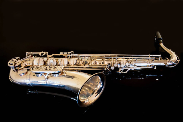 Tenor saxofónico. Woodwind Classical Instrument. Jazz, blues, clásicos. Música. Saxofón sobre fondo negro. Superficie de espejo negro. Estilos musicales
 - Foto, Imagen