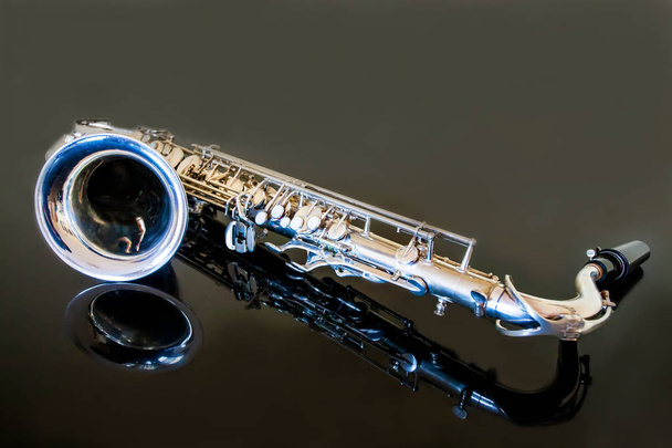 Um tenor saxofone. Woodwind Classical Instrument. Jazz, blues, clássicos. Música. Saxofone sobre fundo preto. Superfície do espelho preto. Estilos musicais
 - Foto, Imagem