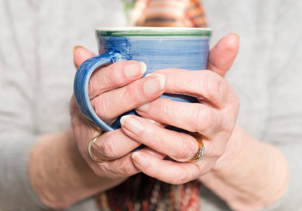 As mãos da mulher idosa segurando uma bebida quente
 - Foto, Imagem