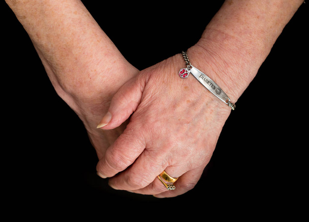Elderly woman's hands with medical alert bracelet for diabetes. - Photo, image