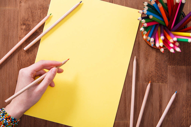 Girl hand drawing, blank yellow paper and colorful pencils on wooden table - 写真・画像