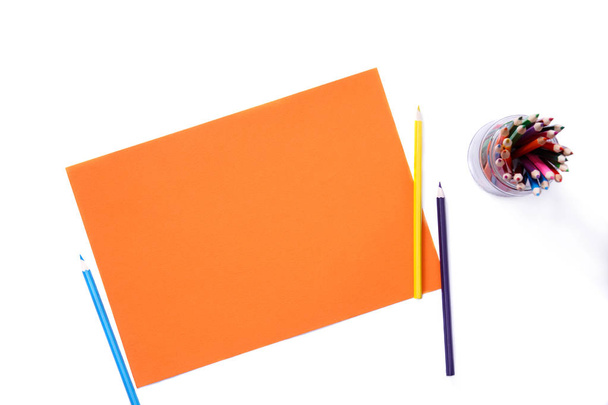 Trozo de papel naranja con lápices de colores sobre fondo blanco aislado
 - Foto, imagen