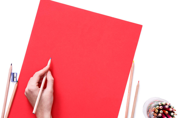 Female hand is ready for drawing with blue pencil on red paper. Isolated on white. - 写真・画像