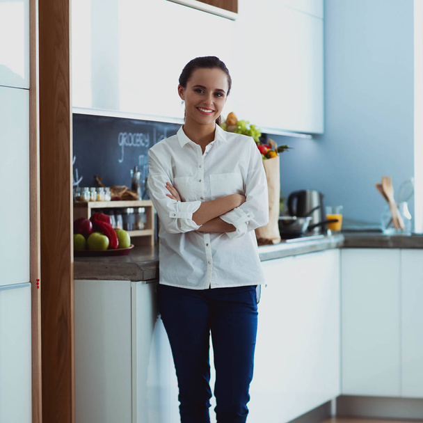 Portret van jonge vrouw staan met armen gekruist tegen keuken achtergrond - Foto, afbeelding