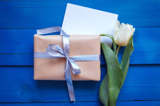 Spring tulip flowers, gift box and paper card on blue wooden table from above in flat lay style.  - Foto, Imagem