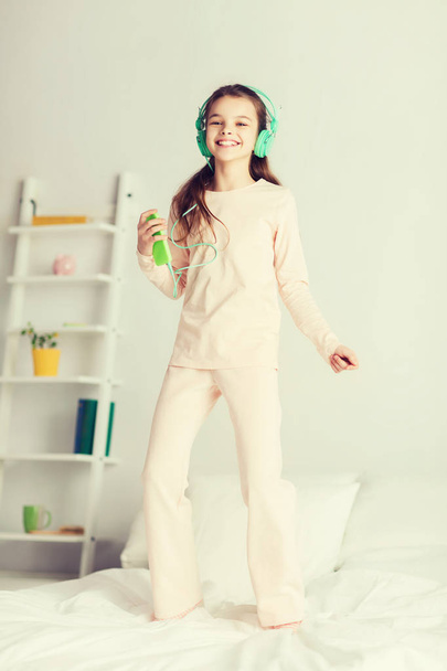 girl jumping on bed with smartphone and headphones - Valokuva, kuva