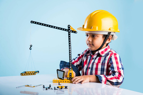 cute indian baby boy playing with toy crane wearing yellow construction hat or hard hat, childhood and education concept - Foto, Imagem