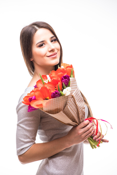 schöne Mädchen im grauen Kleid mit Blumen Tulpen in den Händen auf einem hellen Hintergrund - Foto, Bild