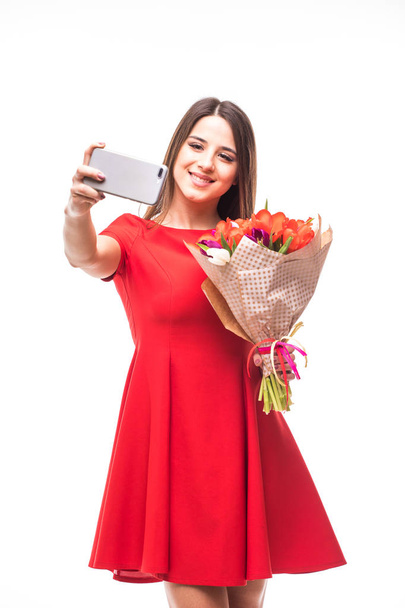 Smiling girl standing with a bouquet of colored tulips in their hands, make selfie phone on white - Fotoğraf, Görsel