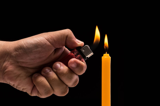 Hand holding burning gas lighter to light candle. Studio shot is - Photo, Image