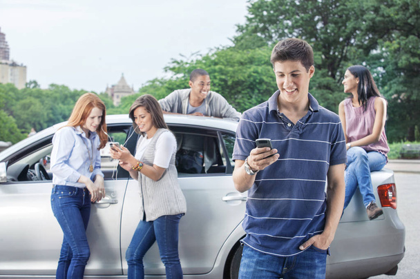 Teini-ikäiset käyttävät matkapuhelimia auton lähellä
 - Valokuva, kuva