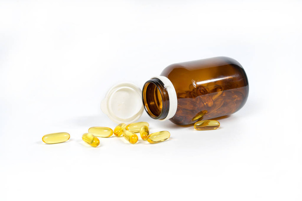 Visolie capsules met omega-3 en vitamine D in een glazen fles, gezonde voeding concept, geïsoleerd op een witte achtergrond. - Foto, afbeelding