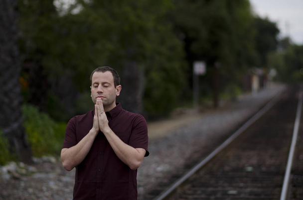 Hombre rezando solo cerca de las vías del ferrocarril al atardecer
. - Foto, imagen
