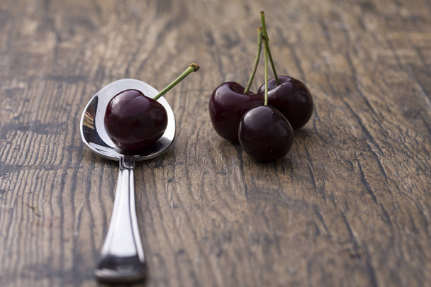 Close-up of cherries in a silver spoon on brown background - Photo, Image
