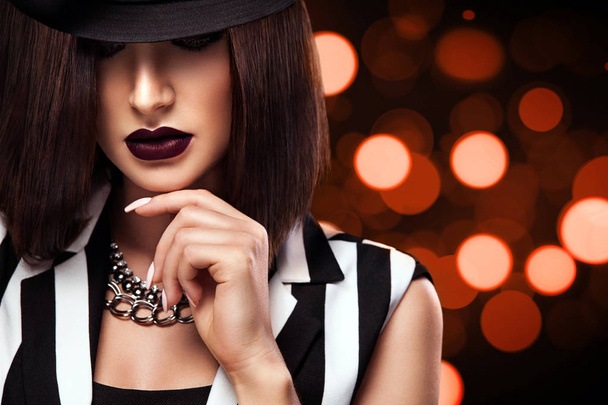 Fashion photo of beautiful young lady in black hat on bokeh lights background. Perfect face makeup. - 写真・画像