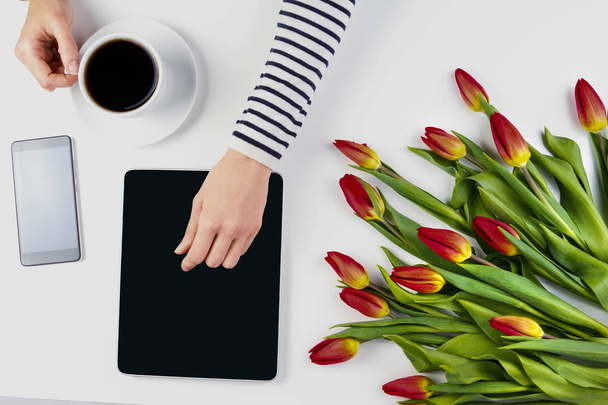 Жінка руки з планшетом, чашкою кави, мобільним телефоном і красивими букетами квітів на білому офісному столі
 - Фото, зображення