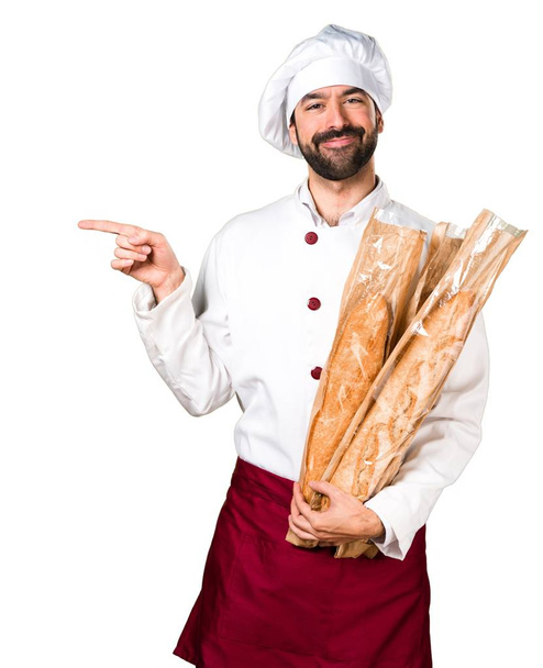 Young baker holding some bread and pointing to the lateral - Fotó, kép
