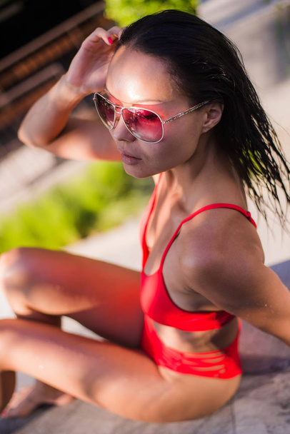 Close up summer portrait of Woman enjoy relaxing in the pool.Beautiful brunette hair sexy woman young girl model in sunglasses and elegant red sexy swimsuit lingerie with around the pool - Zdjęcie, obraz