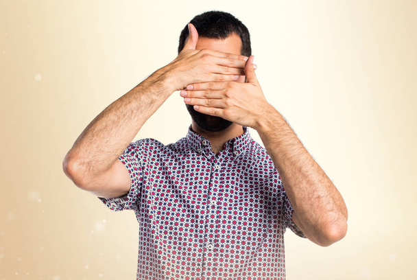 Handsome man covering his face on ocher background - Photo, Image
