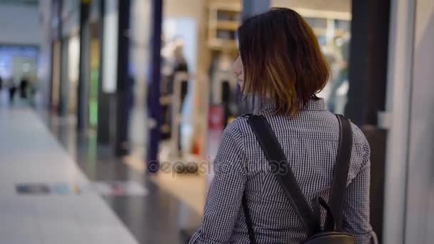 ein junges, schönes kleines Mädchen geht durch ein riesiges Einkaufszentrum an den Schaufenstern vorbei. das Mädchen ist auf der Suche nach einer geeigneten Abteilung für sich selbst, sie geht einkaufen, sie will Geld ausgeben - Filmmaterial, Video