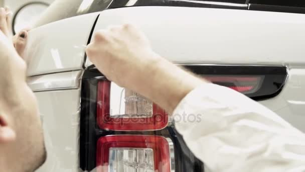 Κοντινό πλάνο των χεριών ενός ανθρώπου που ξεφλουδίζει το φιλμ από ένα άσπρο αυτοκίνητο. - Πλάνα, βίντεο