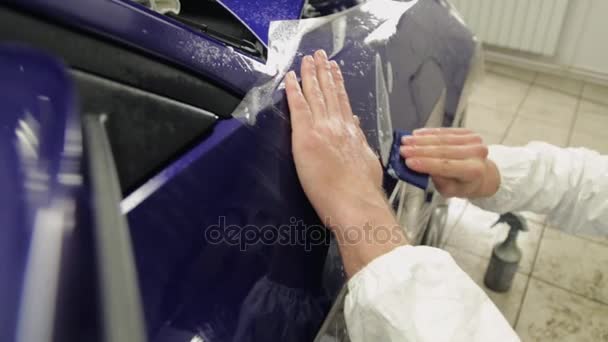Close-up shot van mans handen bij het tankstation plakken vinyl op blauwe auto. - Video
