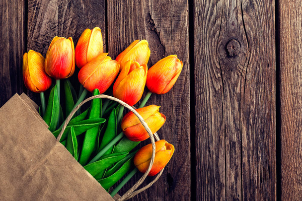Kytice z tulipánů v papírové shopping bag na dřevěné pozadí, koncept slev a prodej na den, den matek či velikonoční žen - Fotografie, Obrázek