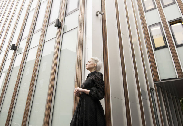 Ευρεία γωνία προβολής, γυναίκα στο μακρύ μαύρο φόρεμα με λευκό κοντό κούρεμα, κτίριο - Φωτογραφία, εικόνα