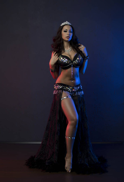 Sexy slim woman, belly dancer in black costume with crystals. Dark background with pink and blue lightening - Photo, Image