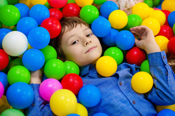 Happy boy having fun in ball pit on birthday party in kids amusement park and indoor play center. Child playing with colorful balls in playground ball pool. Activity toys for little kid - Zdjęcie, obraz