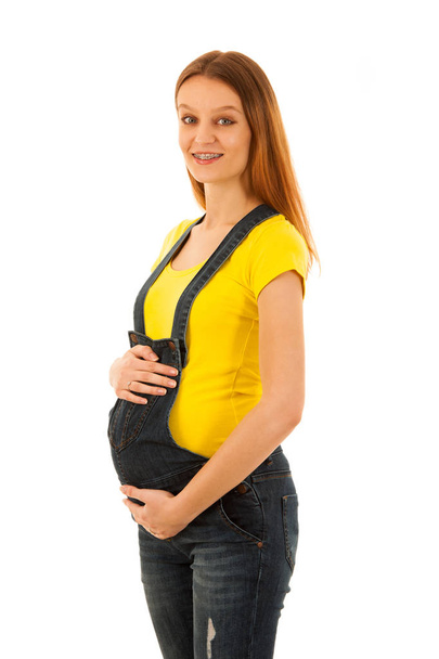 Pregnant woman in yellow t shirt and jeans isolated over white b - Фото, изображение