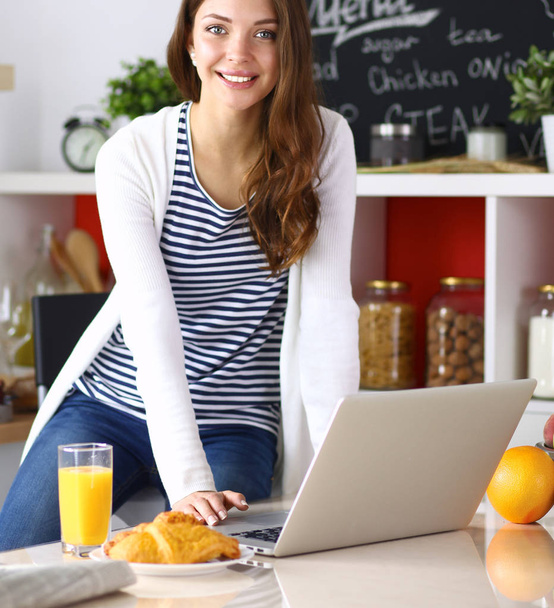 Attractive young woman using laptop and sitting in the kitchen - Fotografie, Obrázek